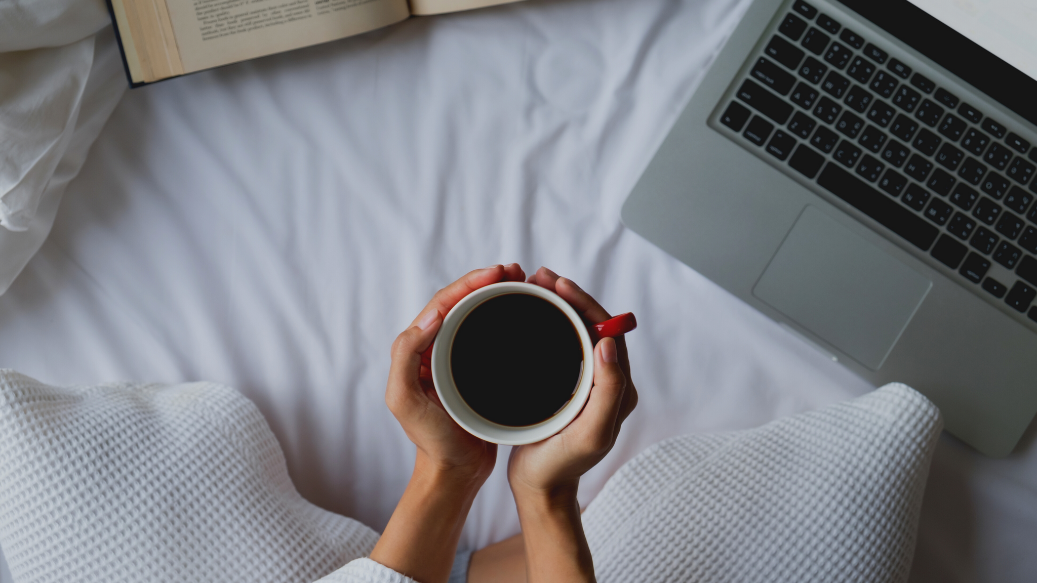 hands holding cup of coffee in bed with computer